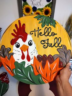 a hand holding up a painted sign that says hello fall with a rooster and sunflowers