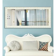 a white couch sitting under a mirror in a living room next to a blue wall