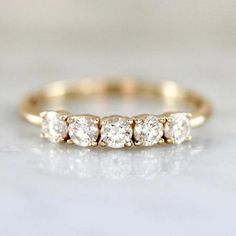 a three stone diamond ring on a white surface with the top half in yellow gold