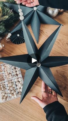 two hands reaching for an origami star on a wooden table with other decorations