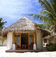 a thatched roof hut on the beach with chairs and tables in front of it