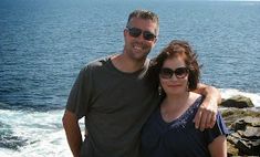 a man and woman standing next to each other near the ocean with their arms around each other