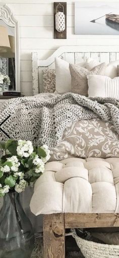 a bed with pillows and blankets on top of it next to a vase filled with flowers