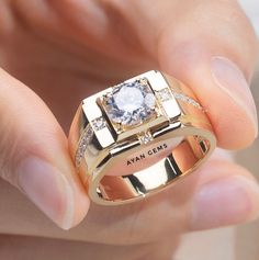 a close up of a person's hand holding a gold ring with a diamond