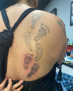 the back of a woman's shoulder with baby footprints on it