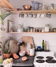 a stove top oven sitting inside of a kitchen next to a wooden shelf filled with pots and pans