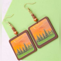 “Fiery Mountain Sunset” Picturesque Scenic Artwork Artsy Evergreen Trees Sliver Moon Framed Picture Faceted Orange Bead Nature Woodsy Forest Outdoorsy Granola Climb Hike Hippie Boho Dangle Earrings. Beautiful Picturesque Scene Little Framed Piece Of Artwork For Your Ears! A Fiery Orange Sunset With A Sliver Moon Hangs In The Sky Above A Row Of Green Evergreen Trees. Three Faceted/Sparkle Orange Beads Are Above The Painting/Image. Very Lightweight. New. Measurements: Eardrop Length: 2.8” Earring Artisan Hand Painted Orange Jewelry, Artisan Hand-painted Orange Jewelry, Earthy Orange Jewelry Gift, Artsy Orange Drop Earrings, Earthy Orange Jewelry As Gift, Nature-inspired Orange Jewelry Gift, Artistic Hand Painted Brown Jewelry, Nature-inspired Orange Jewelry For Gifts, Artistic Handmade Orange Jewelry