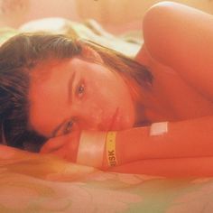 a beautiful woman laying on top of a bed with her arm around her neck and wristband