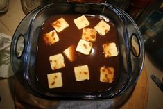 a pan filled with brown liquid and cubes of food on top of a wooden table