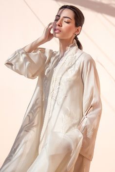 An ivory woven fabric is artfully embroidered with foliage imagery and cutout sleeves that create interest. The ensemble is paired with a matching organza dupatta and a raw silk panwar. Satin Silk Suit, Cutout Sleeves, Boring Outfits, Lace Suit, Pakistani Suit, Latest Dress Design, Fancy Kurti, Desi Clothes, Unique Dress