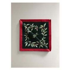 a black and red square with holly leaves on it, hanging from the wall in front of a white wall