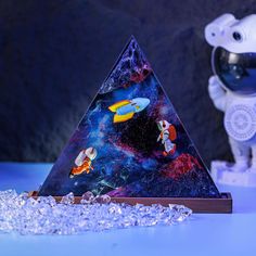 a space themed glass pyramid with fish and astronaut figures in front of it on a blue surface