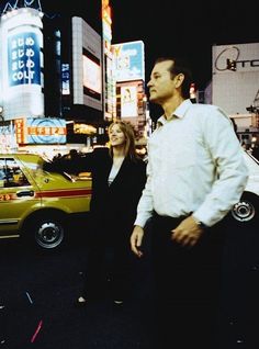 a man and woman standing in the middle of a busy city street at night time