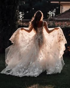 a woman in a white dress is walking through the grass with her arms spread out