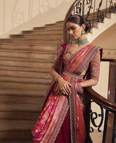 a woman in a red and gold sari standing next to some stairs with her hands on her hips