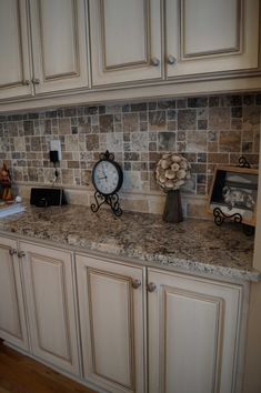 there is a clock on top of the counter in this kitchen with white cupboards