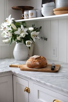 a loaf of bread sitting on top of a cutting board next to a vase with flowers