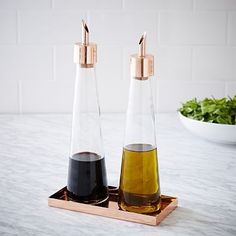 two bottles filled with liquid sitting on top of a wooden tray next to a bowl