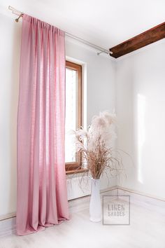 a white vase with some flowers in it next to a pink drapeed window