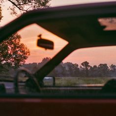 the sun is setting behind a red car with a bird on it's windshield