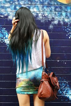 a woman standing in front of a blue wall holding a brown purse and looking at her cell phone