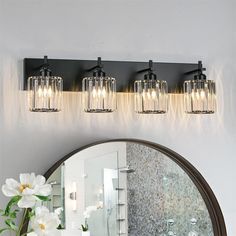 a bathroom vanity with three lights and a mirror on the wall next to a flower vase