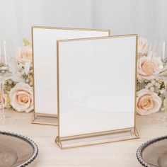 two empty frames on a table with flowers and wine glasses in the background, along with champagne flutes