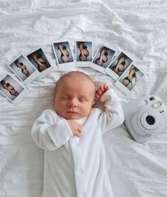 a baby laying on top of a white bed next to polaroid pictures and a camera