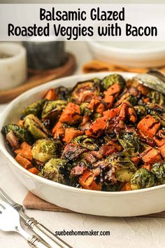 a white bowl filled with roasted veggies on top of a table next to silverware