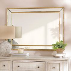 a mirror sitting on top of a white dresser next to a lamp and a vase