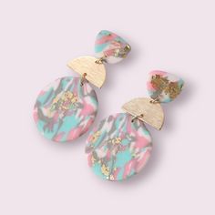 two pink and blue earrings with gold accents on top of each earring, one in the