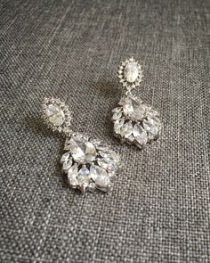 a pair of earrings sitting on top of a gray cloth covered table next to a black and white wall