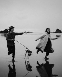 a man and woman are walking their dog on the beach