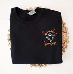 Our new Spooky Season Halloween Sweatshirt is the perfect addition to your Fall and Halloween wardrobe. This embroidered sweatshirt is professionally embroidered and will definitely get you excited for Fall and Halloween!  Professionally embroidered with left chest placement.  Sweatshirt is a 8 oz. 50/50 cotton/polyester blend fleece Spooky season will be embroidered with our premium orange thread. The ghost will be embroidered with black thread on the following colors - White, Sand, Light Blue, Black Cotton Halloween Sweater, Black T-shirt With Embroidered Logo For Fall, Black Embroidered Logo T-shirt For Fall, Black Sweatshirt With Custom Embroidery For Fall, Black T-shirt With Custom Embroidery For Fall, Embroidered Black T-shirt For Fall, Black Embroidered T-shirt For Fall, Halloween Long Sleeve Sweatshirt With Custom Embroidery, Black Embroidered Tops For Halloween