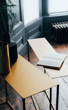 two tables with books and vases on them in front of a window, next to a plant