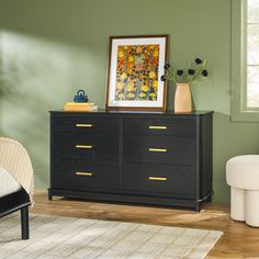 a black dresser in a green room with white chairs and a painting on the wall