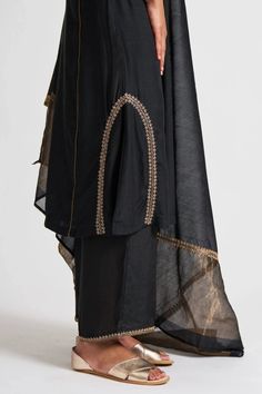 Black asymmetric hem A line kurta in hand embroidered dabka work. Paired cotton silk palazzo with floral embroidered hem and sheer chanderi dupatta broad gold hem.
Component: 3
Pattern: Hand embroidered
Type Of Work: Thread work, Gota patti
Neckline: High neck
Sleeve Type: Three quarter
Fabric: Cotton silk, Chanderi
Color: Black
Other Details: 
Piping detail
Side pocket
Occasion: Sangeet ,Work - Aza Fashions Dabka Work, Kurta Palazzo Set, Chanderi Dupatta, Embroidered Hem, A Line Kurta, Palazzo Set, Thread Work, Designer Gowns, Embroidered Silk