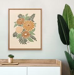 an art print hangs on the wall next to a potted plant in front of a cabinet