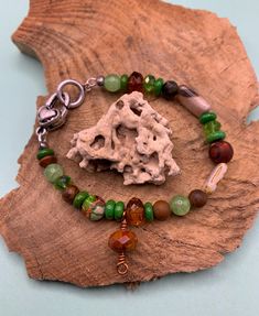 I used a collection of different shapes and sizes of green beads and some brown beads for contrasting colors.  The focal bead is Venus jasper and a smaller focal bead of ivory travertine with a brown wash.  Perfect for the fall season, St. Patrick's Day, or as a gift for the upcoming holidays. Brown Beaded Bracelets For Healing, Nature-inspired Green Jewelry With Wooden Beads, Healing Brown Beaded Bracelets With Colorful Beads, Green Heart Beads Bracelet, Green Heart Beads Bracelet Jewelry, Earthy Green Bracelets For Healing, Earthy Green Bracelet For Healing, Earthy Green Healing Bracelet, Green Round Beads Bracelet, Nature-inspired