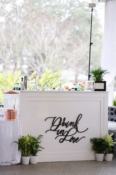 a white counter topped with potted plants next to a sign that says drink my love