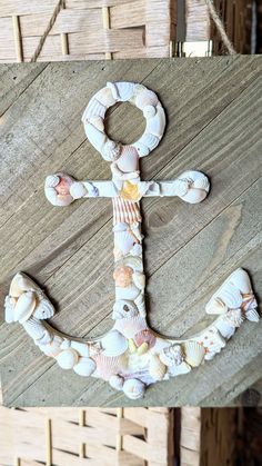 an anchor made out of seashells is hanging on a wooden board with rope