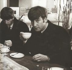 two men sitting at a table with cups in their hands and plates on the table