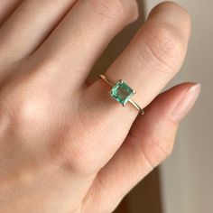 a woman's hand holding an emerald ring