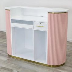 a pink and white cabinet with gold trim on the bottom, against a wooden floor