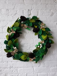 a wreath made out of felt and leaves on a white brick wall with greenery