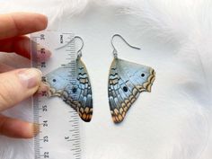 a close up of a person's hand holding a pair of butterfly shaped earrings