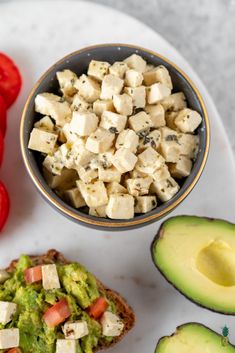 an avocado, tomato and tofu salad on a white plate next to sliced red peppers