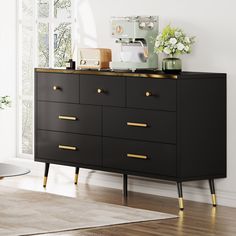 a black and gold dresser with flowers on top in a white living room, next to a window