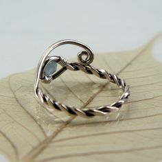 A silver and aquamarine ring with a twist and open spiral design. It's adjustable and perfect as a gift if you're not quite sure of the size you need. The shank is twisted from one wire and in the loop at the end is nestled a round faceted aquamarine bead. This version is milky which highlights the colour wonderfully and reminds me of frozen lakes and ice skating. Versions with a clear aquamarine and with moss aquamarine are also available in my shop. The opposite end from the gem is shaped into Modern Twist Twisted Jewelry Gift, Handmade Modern Promise Ring Jewelry, Handmade Modern Promise Ring, Modern Twist Jewelry With Gemstone For Gift, Modern Twist Silver Wire Wrapped Jewelry, Adjustable Blue Topaz Birthstone Jewelry, Adjustable Birthstone Jewelry With Blue Topaz, Handmade Adjustable Swirl Jewelry, Adjustable Nickel-free Swirl Jewelry