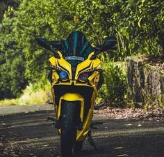 a yellow and black motorcycle parked on the side of a road next to some trees